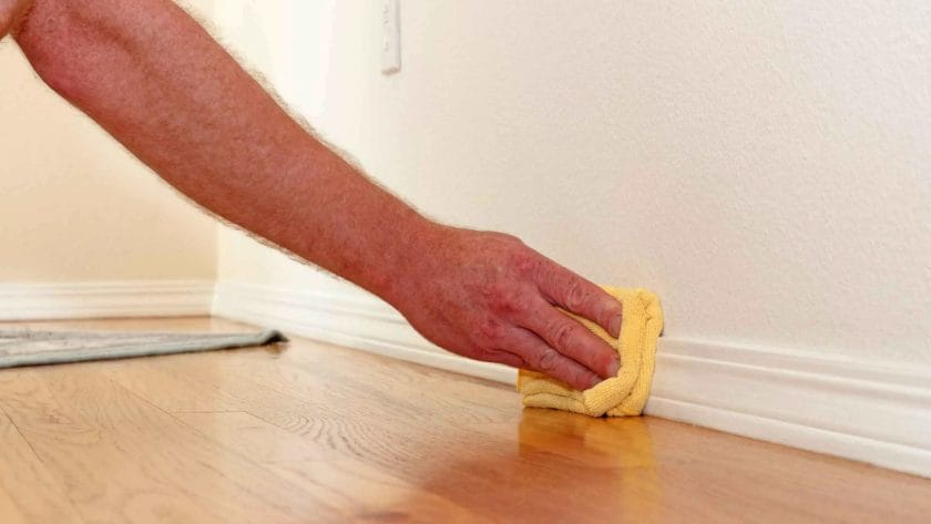 Person's arm cleaning baseboards with a yellow rag. How to Clean Baseboards Without Bending Over?